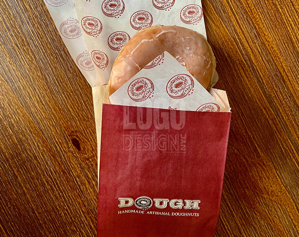 doughnut shop bag visual branding featuring maroon doughnut bag with dough colored lettering and a donut for the O in the logo of Dough Donuts